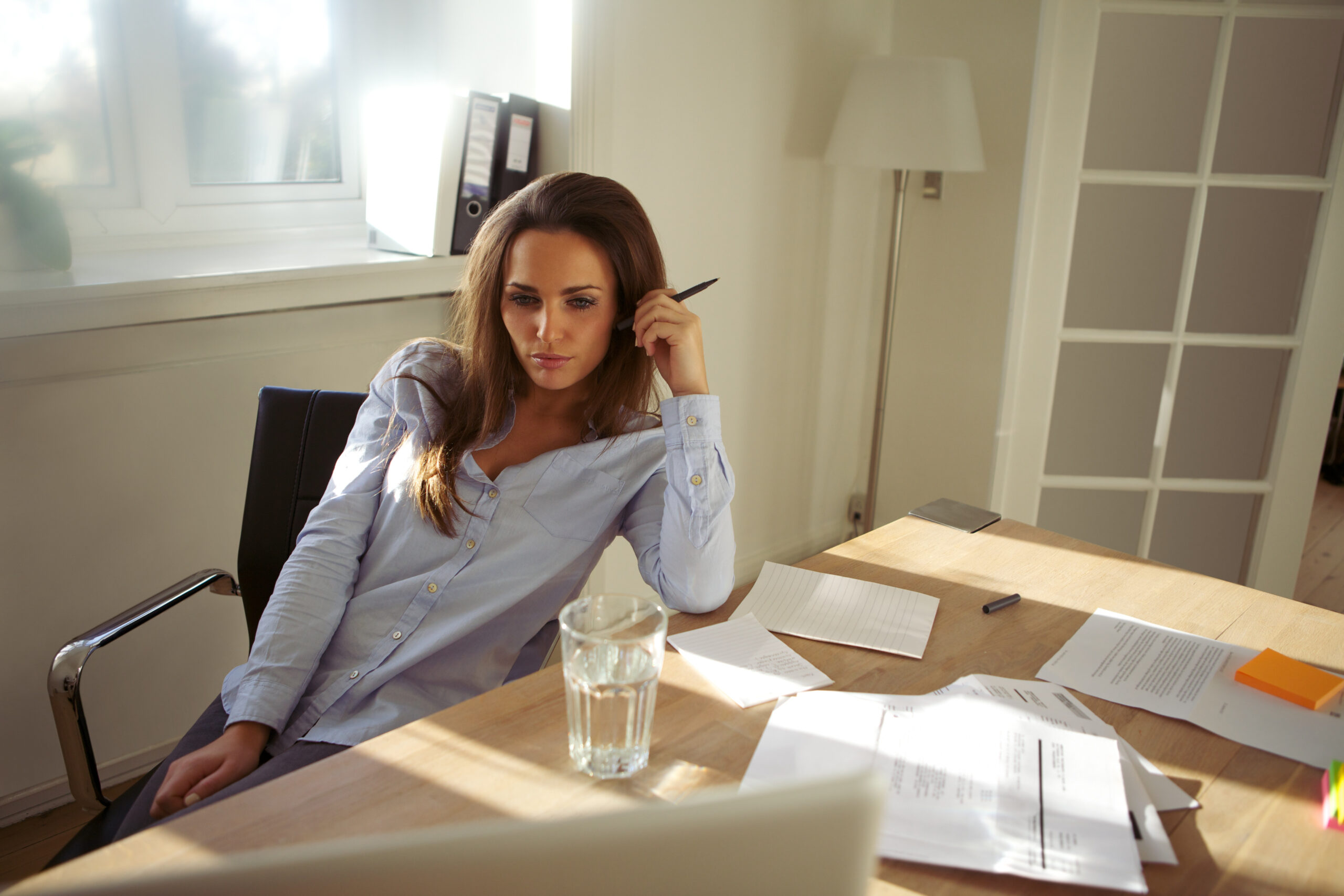 Small business owner sitting at a desk and thinking through marketing and business tasks while working on a laptop.